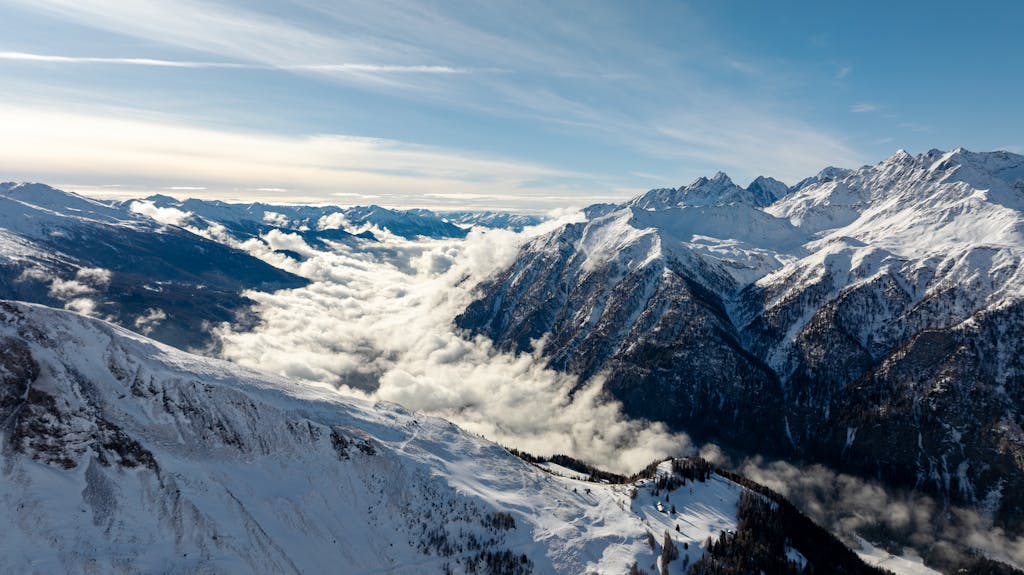 Breathtaking aerial view of snow-capped mountains in Korutany, Austria, with clouds nestled in valleys.